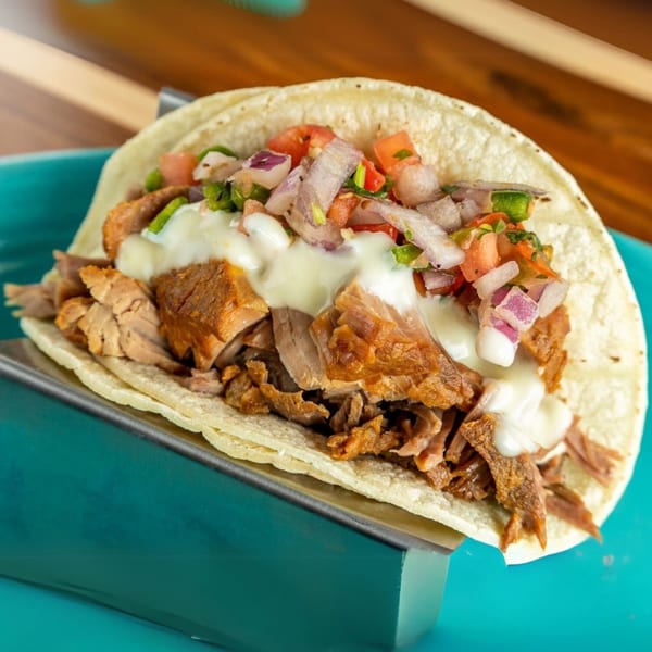 A Cabo Taco with shredded pork, white sauce, and pico de gallo on a blue plate.
