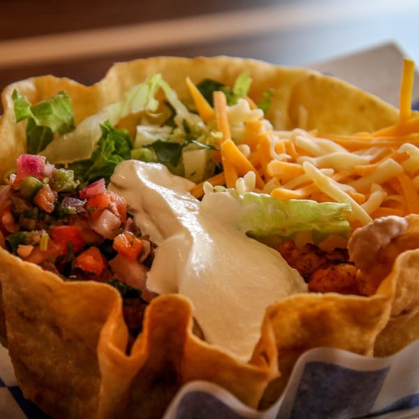 A close-up of a Cabo Taco salad in a crispy tortilla bowl with salsa, cheese, and sour cream.