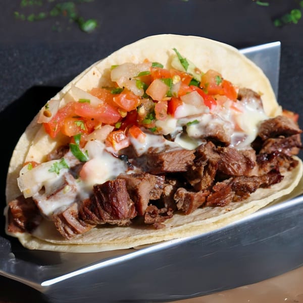 A Cabo Taco carne asada taco, topped with pico de gallo and white sauce, on a metal holder.