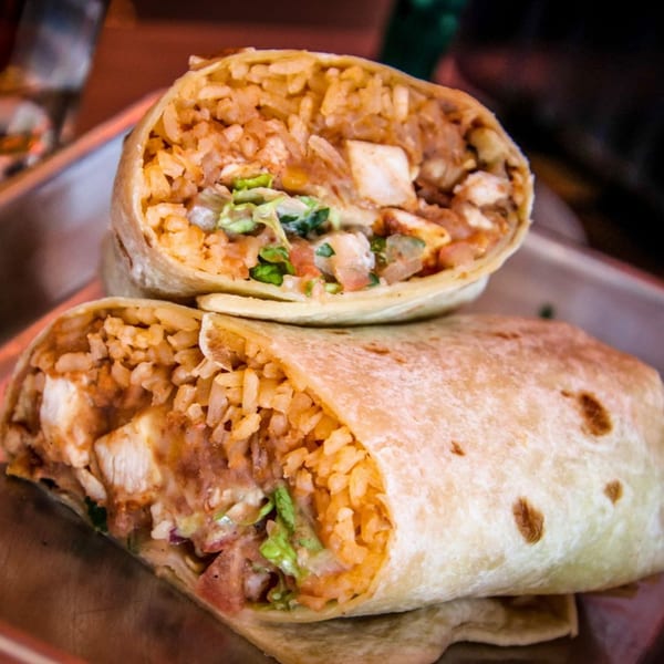 Two large, cut burritos filled with rice, chicken, and fresh salsa on a metal tray.